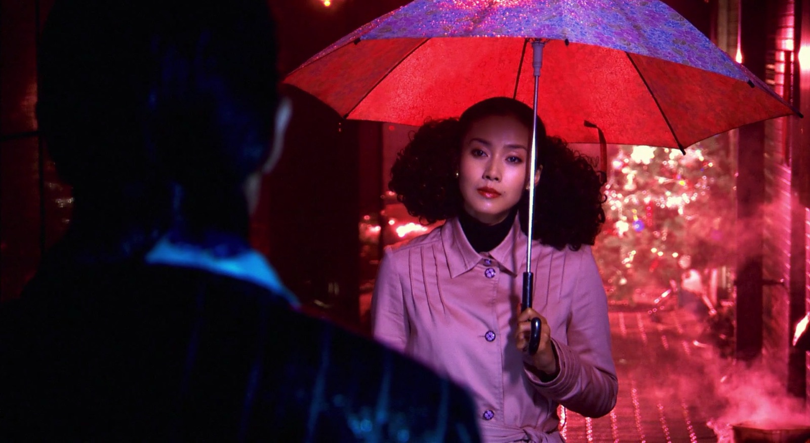 松子撑着红伞站在雨中，灯光映照出她的脸
